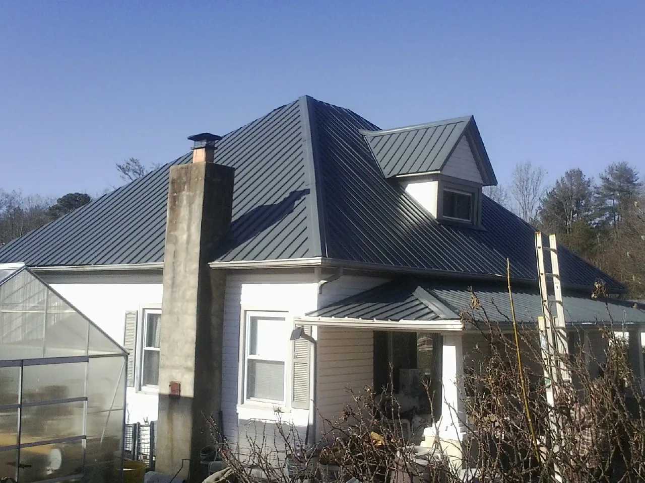 Dark blue standing seam metal roof on a white farmhouse with dormer — Slate & Tile Roof Repair by Roofing Brothers in Rush Valley