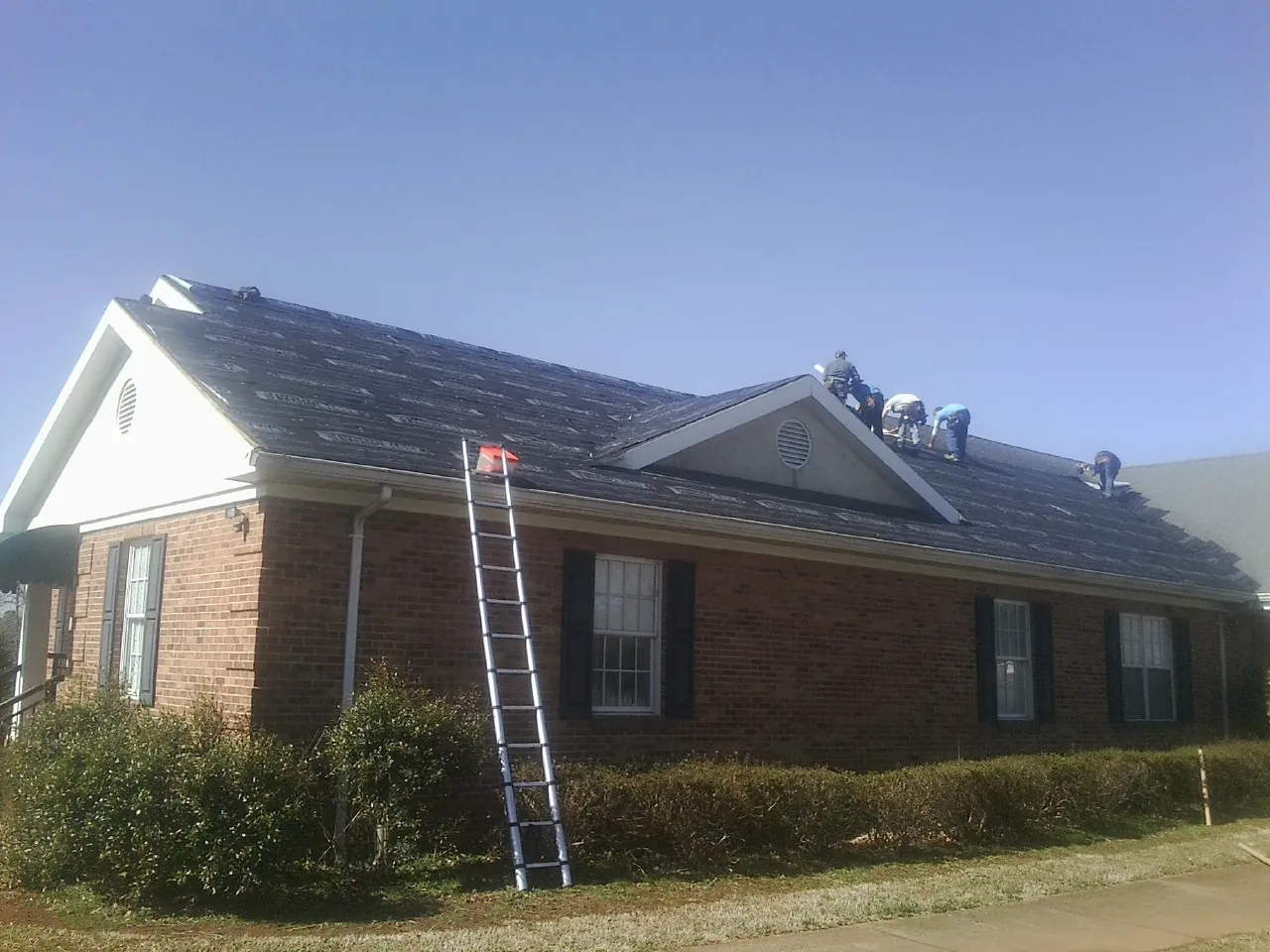 Crew tearing shingles off a brick ranch roof with a ladder set — Emergency Roof Repair work by our crew in Rush Valley