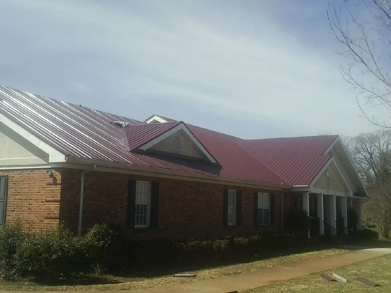 Red metal roof with gabled entries on a long brick building, from a Hail Damage Roof Repair job in Rush Valley