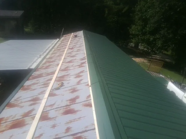 Old rusted panels beside newly installed green metal roofing — Wind Damage Roof Repair by Roofing Brothers in Rush Valley