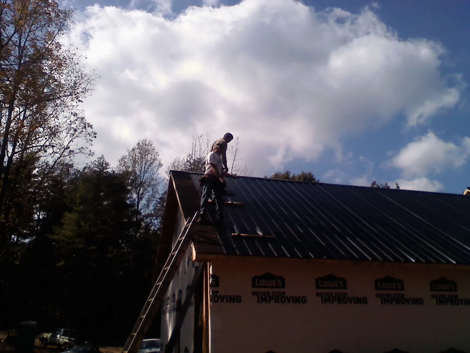 Roofer fastening dark metal panels high against a cloudy sky, from a Roof Inspection job in Rush Valley