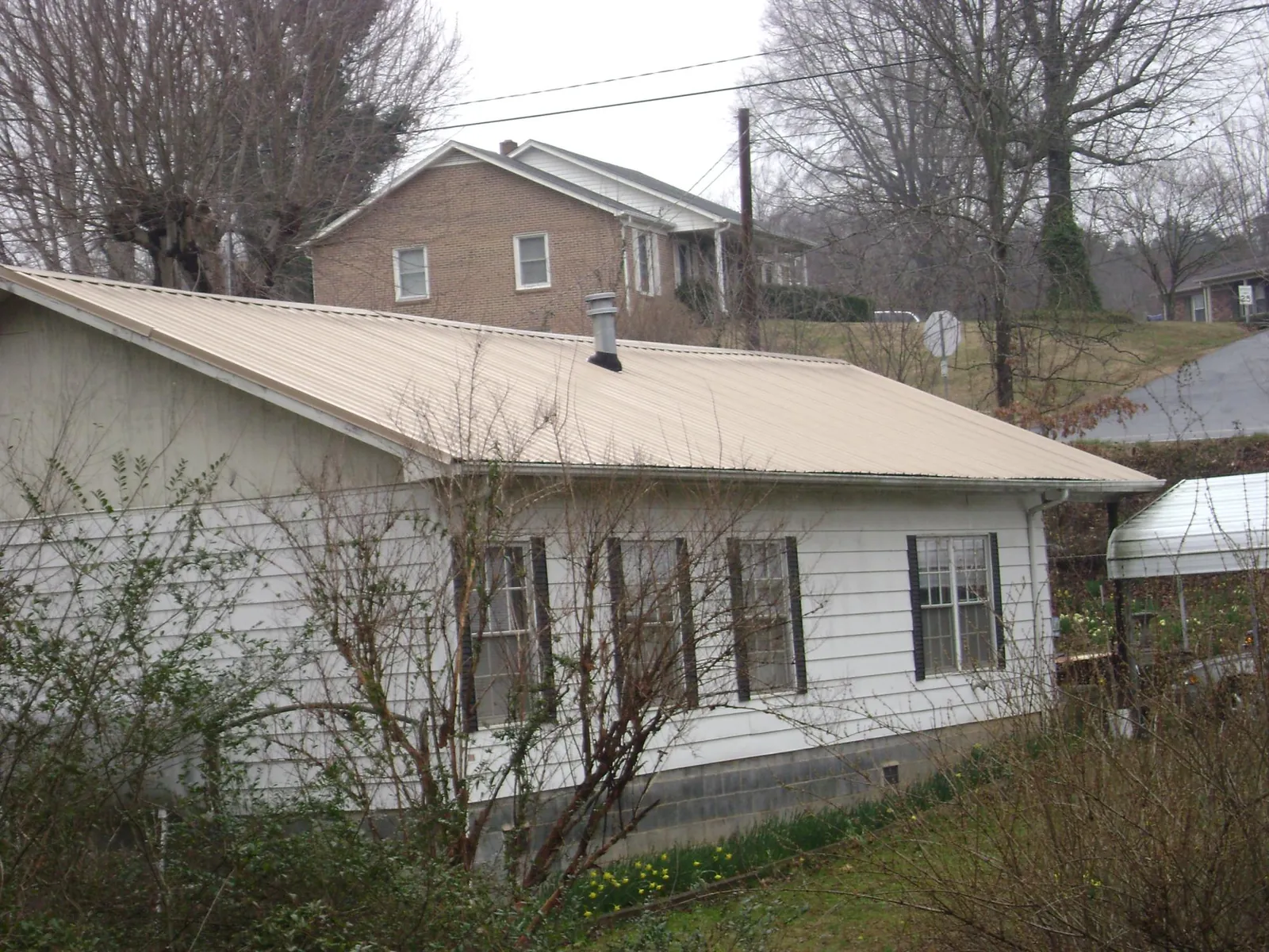 Tan metal roof on a white sided house set into a hillside — Commercial Roofing by Roofing Brothers in Rush Valley