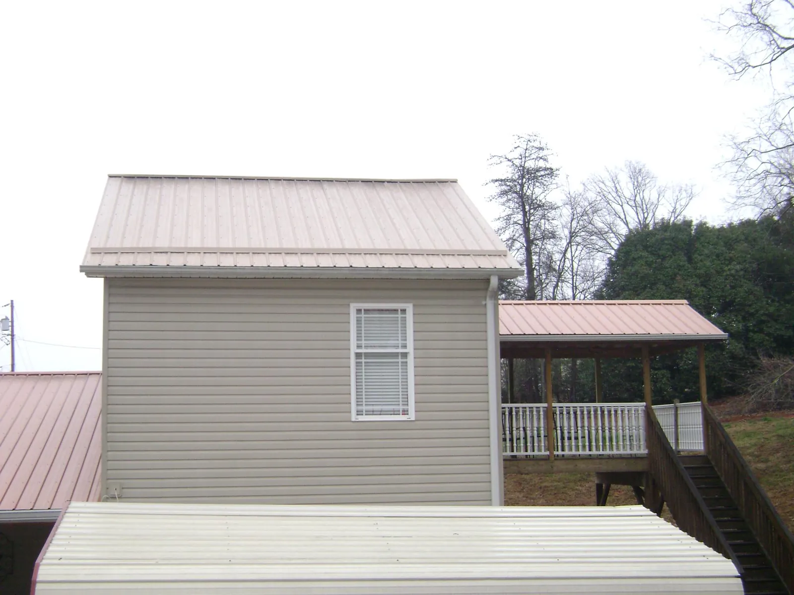 Tan metal roofs on a two story addition and attached porch, from a Roof Replacement job in Rush Valley